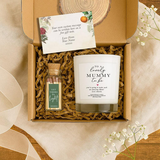 A white soy candle with the message “To a lovely Mummy to Be” and a personalised note, displayed in a kraft gift box with a wood slice, floral gift card, and a match bottle labeled “Let There Be Light”. A thoughtful pregnancy or baby shower gift.