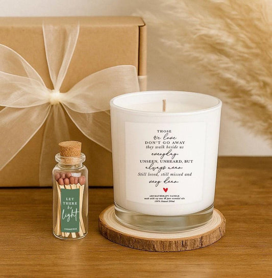 A remembrance candle with a poem that reads “Those we love don’t go away…” printed on a transparent label, placed in a kraft gift box with a rustic wood slice and a match bottle labeled “Let There Be Light”. A thoughtful sympathy or memorial gift.