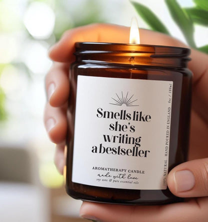 Candle with label that reads 'Smells like she's writing a best seller', 100% Natural Soy Wax Essential Oil aromatherapy candle gift